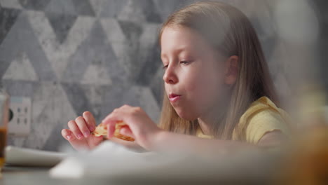 close up of cute child in yellow shirt eating grilled egg cheesy pizza at dining table with soft natural lighting coming through creating warm cozy atmosphere with blurry foreground