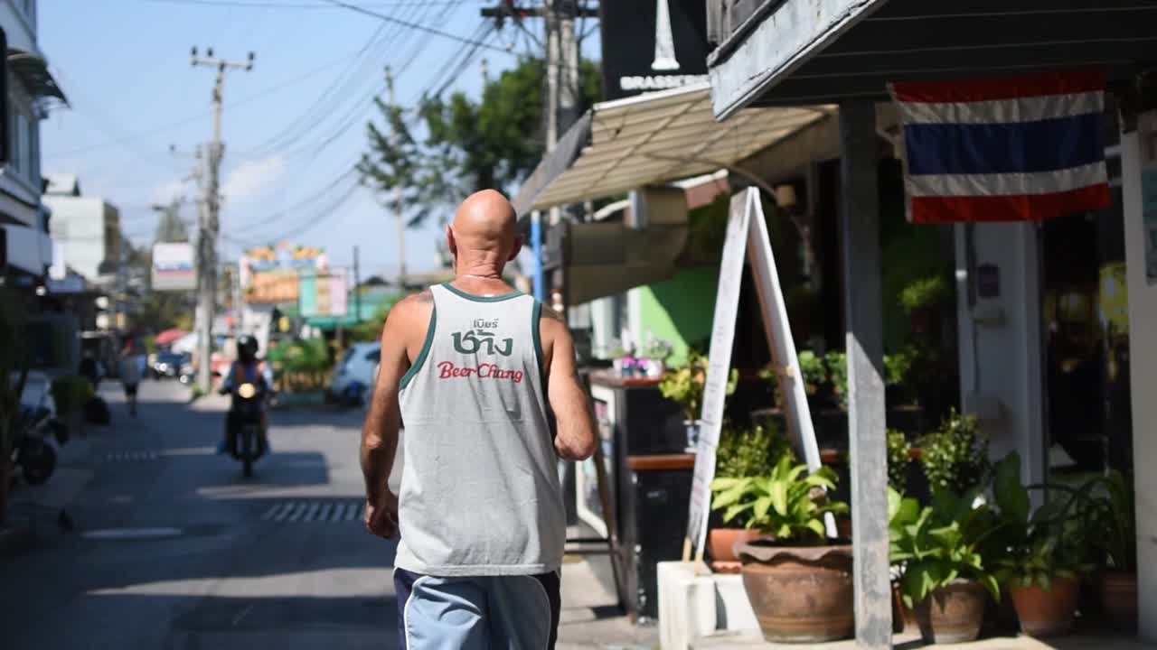 Bald man in tank top walking through Hua Hin street, Thailand, slow motion