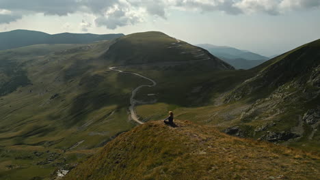 paisaje de carreteras sinuosas a través de colinas verdes y montañas escarpadas, con una persona sentada