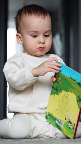 little baby boy focused on the book in his hands. lovely kid sits on the floor trying to open the book. vertical video
