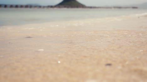 Primer-Plano-De-La-Arena-De-Una-Playa-Mientras-Pequeñas-Olas-Y-Agua-Chocan-Contra-El-Marco