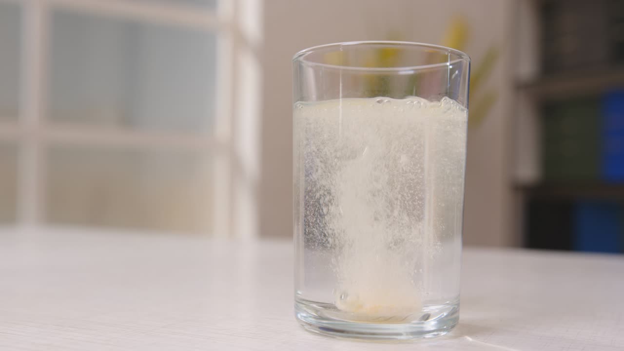 el hombre lanza una pastilla soluble efervescente en un vidrio transparente con agua en la mesa en la habitación de primer plano. proceso de disolución de la pastilla en agua.