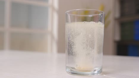 man throws effervescent soluble tablet into transparent glass with water on table in room close-up. process of dissolving pill in water.