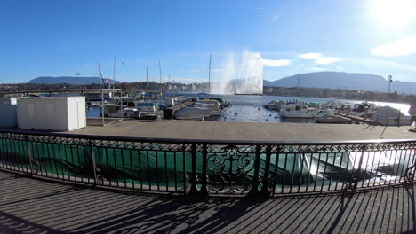 Jet-d'eau-de-Genève-dans-le-vent,-vu-depuis-la-rive-droite,-et-bateaux-en-rade