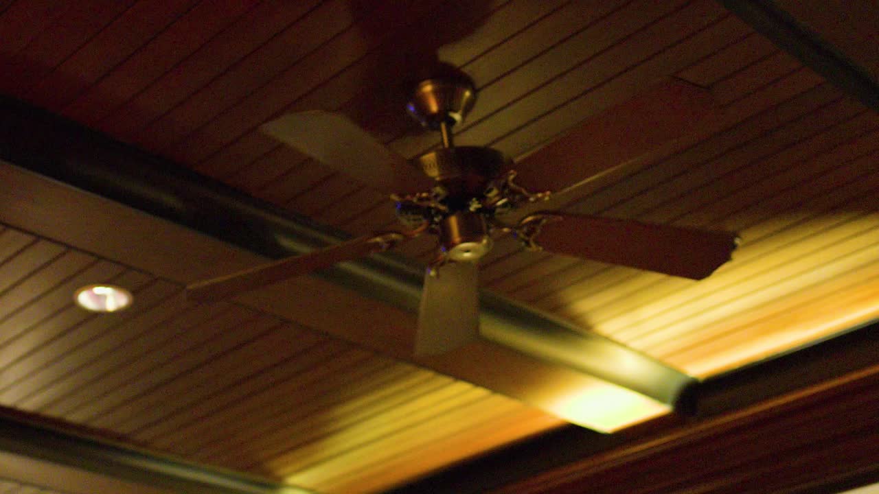 Wooden ceiling fan spins under warm indoor lighting, tropical style, Bangkok, steady upward view