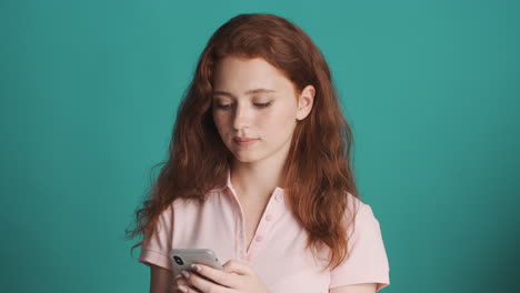 Redheaded girl in front of camera on turquoise background.