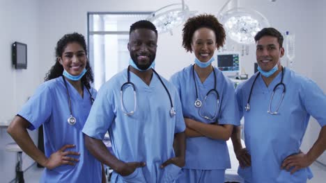 Portrait-of-diverse-male-and-female-doctors-standing-in-operating-theatre-smiling-to-camera