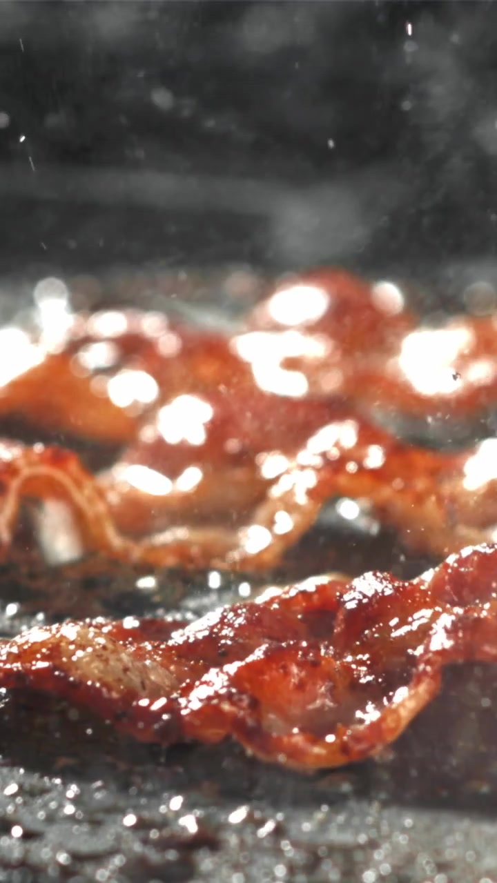 Primo piano di pancetta che sfrigola e frigge su una padella calda