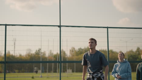 man during volleyball training session throws ball to player in background, slams ball over net, lady in cyan hoodie watching, another lady observing, teamwork and training atmosphere