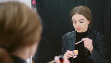 woman applies concealer in front of a mirror
