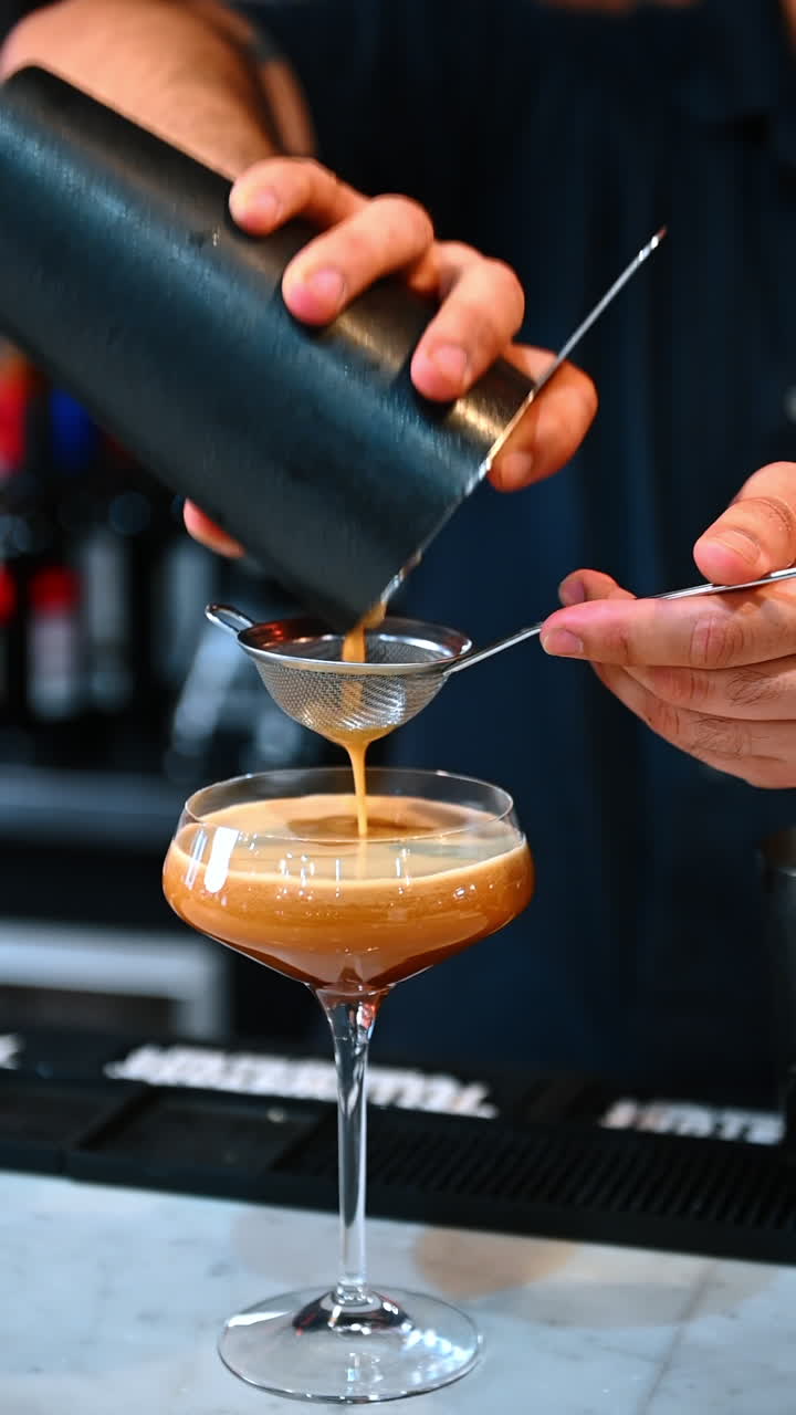 Barista straining creamy cocktail. Kyiv, Ukraine, 23 August 2025: A creamy shaken drink is strained through a mesh into a coupe glass at the bar