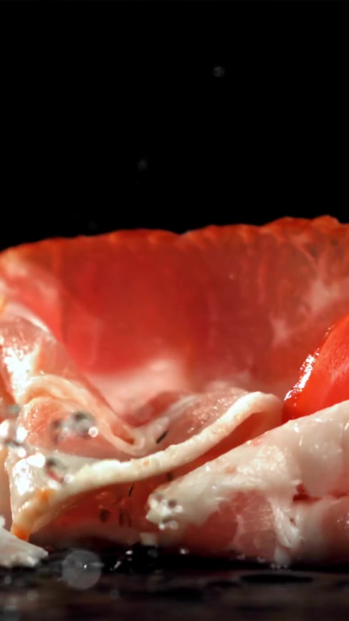 Fette di pancetta cruda che cadono al rallentatore e schizzano acqua.