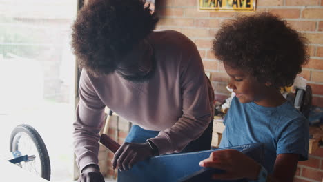 Middle-aged-black-father-and-his-pre-teen-son-standing-at-a-workbench-in-their-garage-talking-as-they-build-a-racing-kart-together,-low-angle