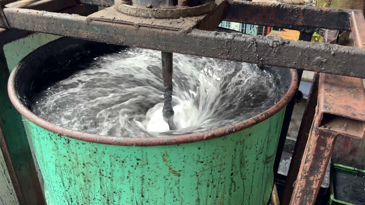 Close-up of an industrial wastewater mixing process, showing a mechanical stirrer creating turbulence inside a large metal tank