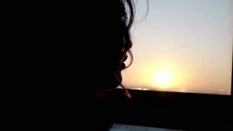 silueta del rostro de la niña mirando por la ventana al atardecer