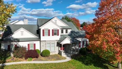 a white house with red shutters, autumn foliage, and a lawn covered in fallen leaves