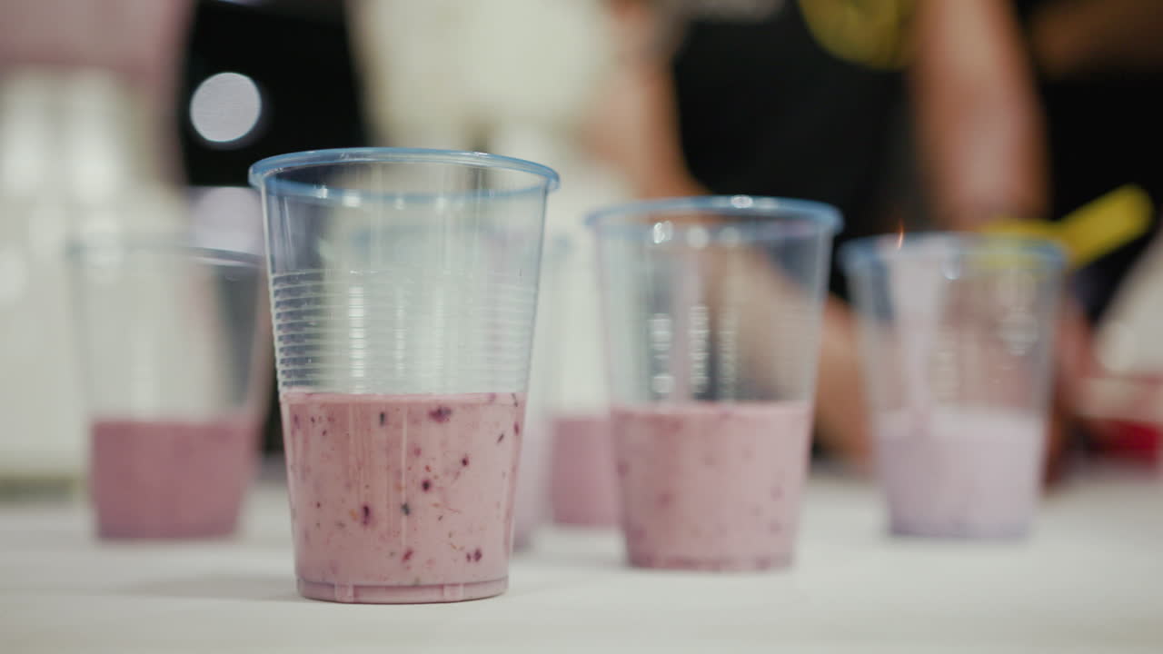 Close up of a couple of cups with tasty healthy and fruity red pink strawberry, blueberry, avocado and raspberry smoothie on a white table top