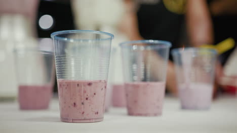 close up of a couple of cups with tasty healthy and fruity red pink strawberry, blueberry, avocado and raspberry smoothie on a white table top