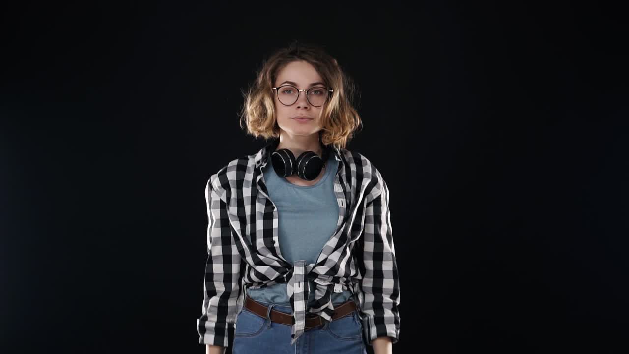 atractiva mujer joven europea soplando labios, enviar un montón de besos de aire aislados en fondo negro en el estudio en ropa casual y auriculares en el cuello. personas emociones sinceras, concepto de estilo de vida