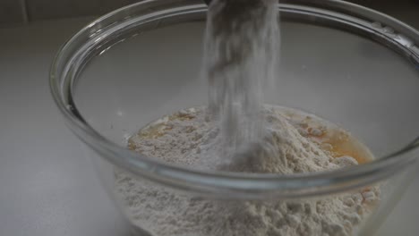 male hand sprinkling baking powder from metal spoon into mix of flour and egg in glass bowl