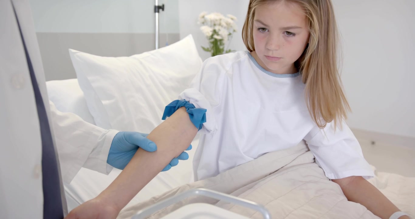 Personale medico che si avvicina al letto, avvolgendo un laccio emostatico blu attorno all'avambraccio di un bambino, assicurando il prelievo di sangue.