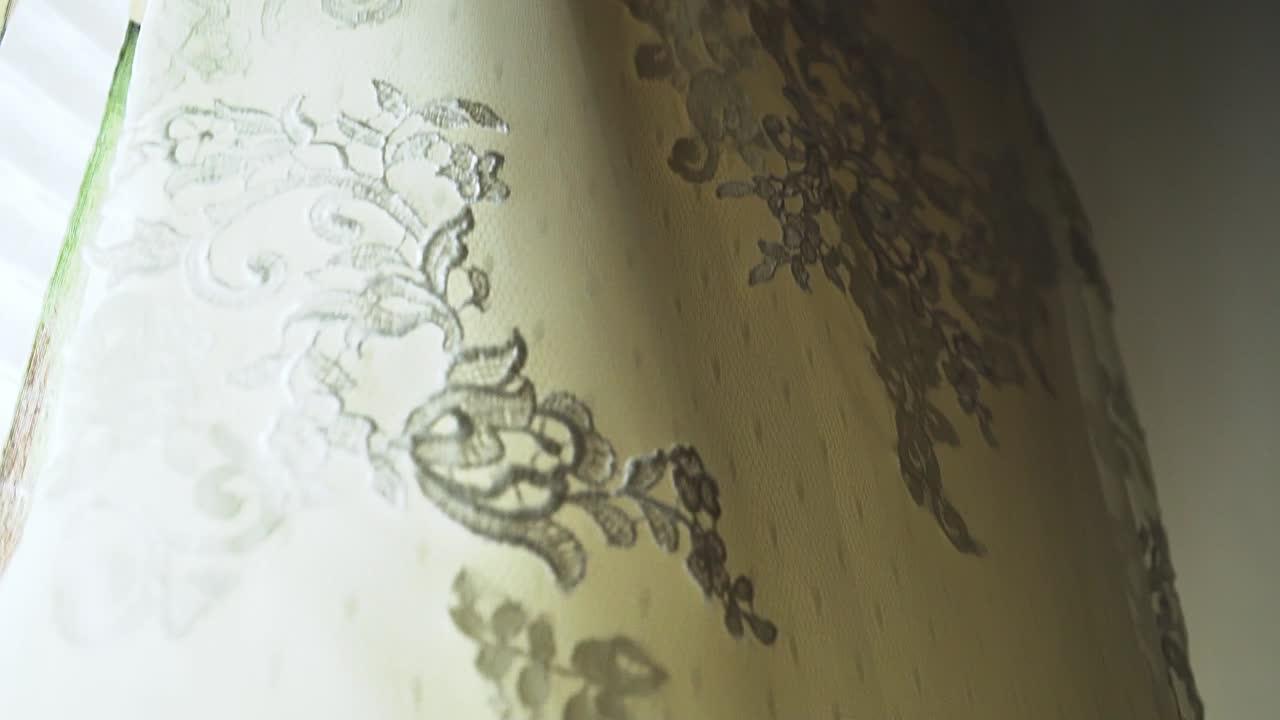 신부와 신랑의 결혼식 전에 햇빛이 비치는 동안 창문에 매달려 있는 하얀 웨딩드레스의 영화 같은 슬로우 모션 하강 핸드헬드 샷