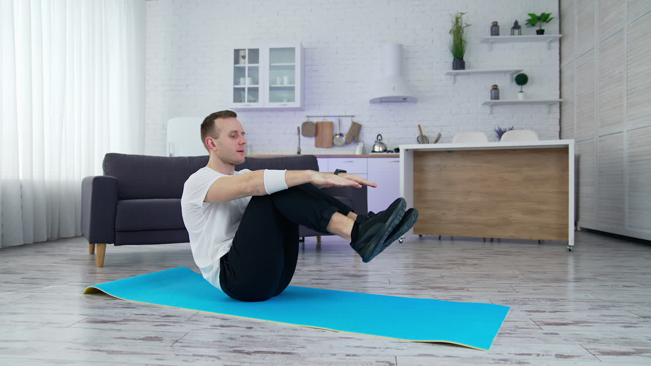 Man doing physical exercise at home. Young man practices on a mat in the modern kitchen during quarantine. Sport at home.