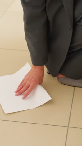 closeup of businesswoman wearing grey trousers and heels standing on tiled office floor with blank white paper sheets scattered around feet suggesting dropped documents