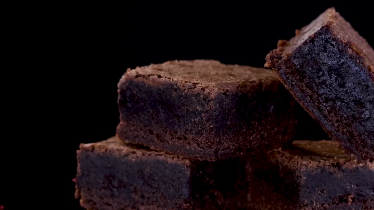 Un primo piano dettagliato di ricchi brownies al cioccolato che ruotano su uno sfondo nero solido.