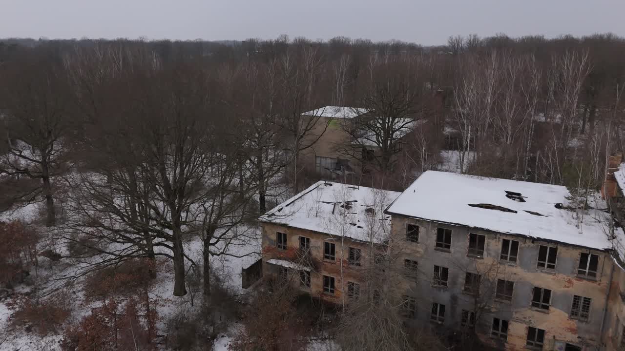 Riprese cinematografiche con drone di un edificio abbandonato dell'era sovietica vicino a Lipsia, Germania. Strutture coperte di neve si ergono ai margini di una foresta, creando una scena invernale tranquilla e suggestiva