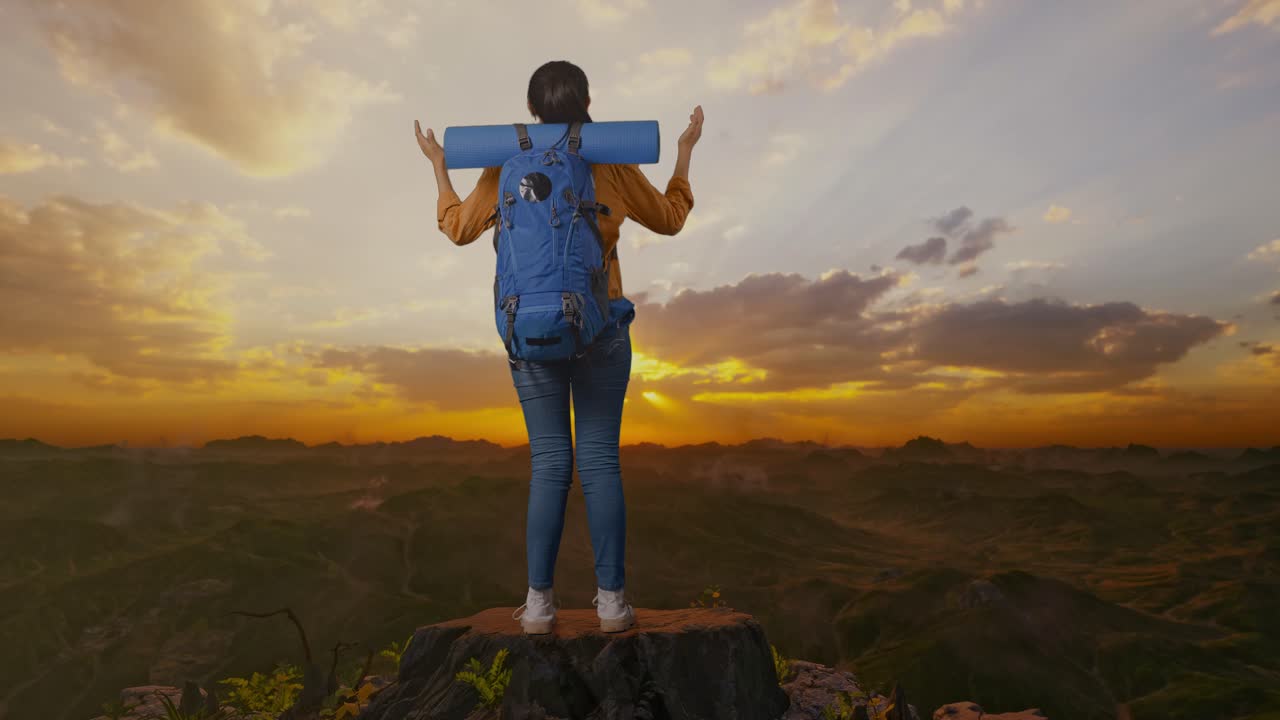vista trasera completa del cuerpo de una excursionista femenina con mochila de montañismo extendiendo los brazos y mirando la vista a su alrededor mientras está de pie en la cima de la montaña durante la hora del atardecer