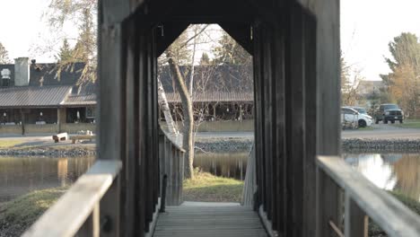 slow motion hand held clip walking across a wood pedestrian bridge that crosses a pond to a island with a reception building in the background