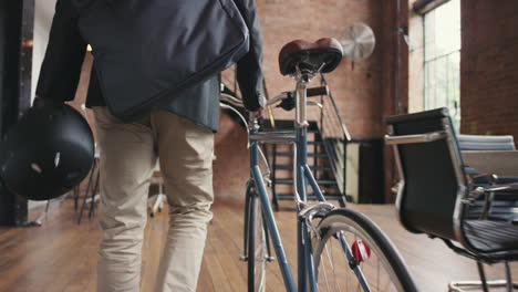 young businessman arriving at work pushing bicycle carrying helmet