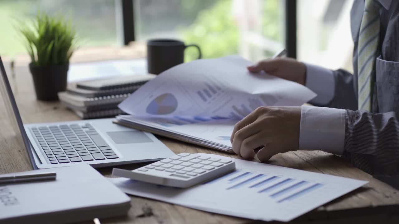 Businessman developing business project and analyzing marketing graph data with accounting documents and financial reports on 4k video table.