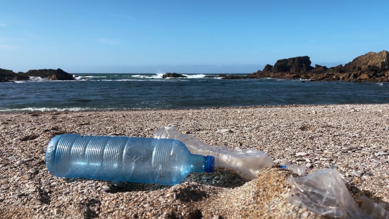 Lähikuva muovisaasteesta rannalla, pullojen ja jätteiden huuhtouduttua rantaan.