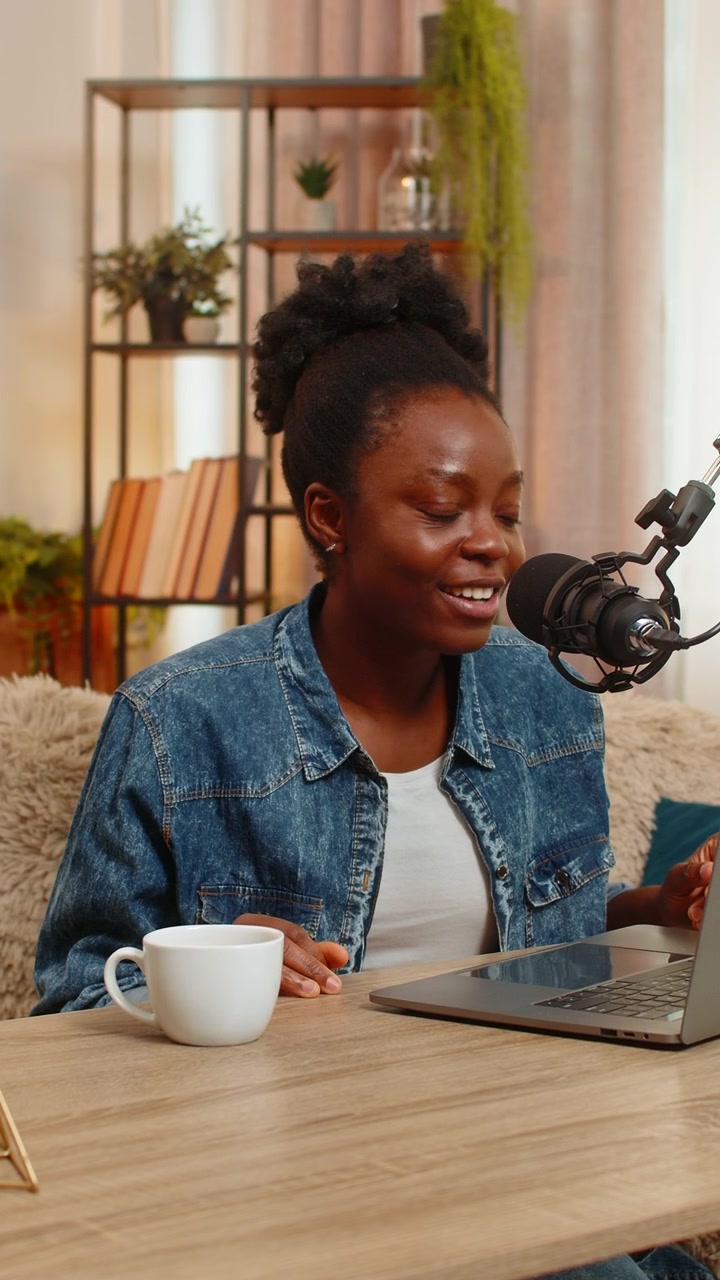 Donna blogger afroamericana che registra un vlog podcast con microfono da studio sorridendo al tavolo di casa