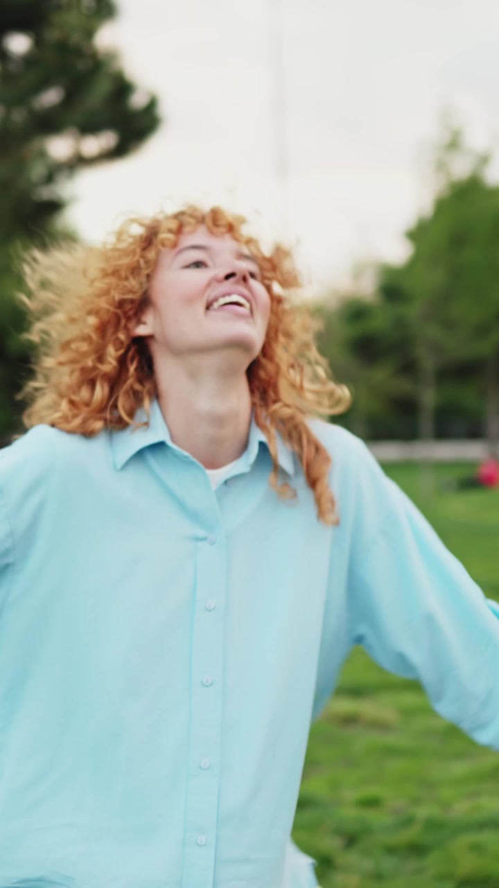 Giovane donna felice con capelli rossi ricci che balla in un parco.