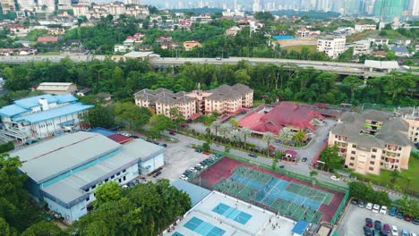 aerial reveal shot transitioning from pickleball courts to the kuala lumpur skyline. the courts are active with players, surrounded by lush greenery and urban buildings, sports with city life malaysia