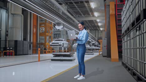 full body side view of an asian female professional worker standing with her laptop in ev car factory, high-tech industrial facility, typing on her laptop's keybaord with meditation