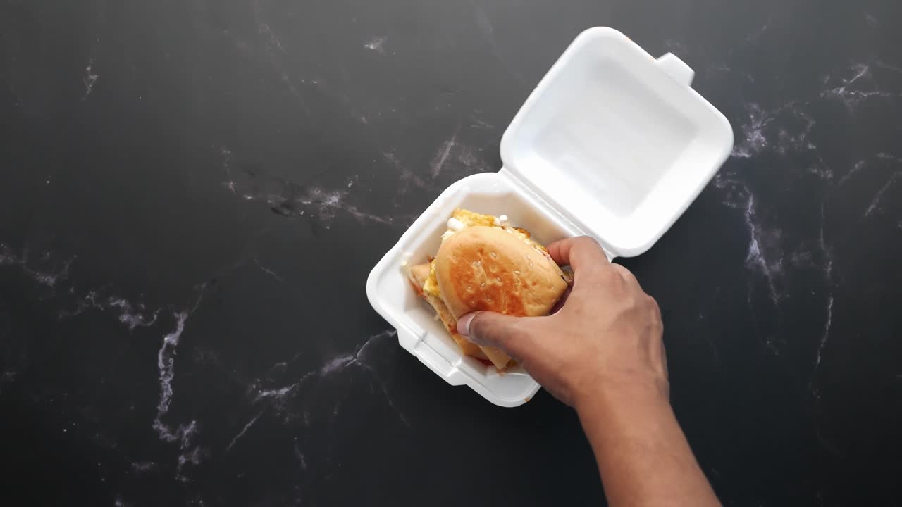 mano sosteniendo un sándwich en una caja de comida para llevar.