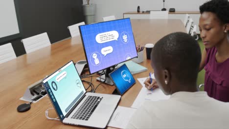 African-american-businesswomen-talking-and-using-technology-with-digital-chat-on-screens-in-office