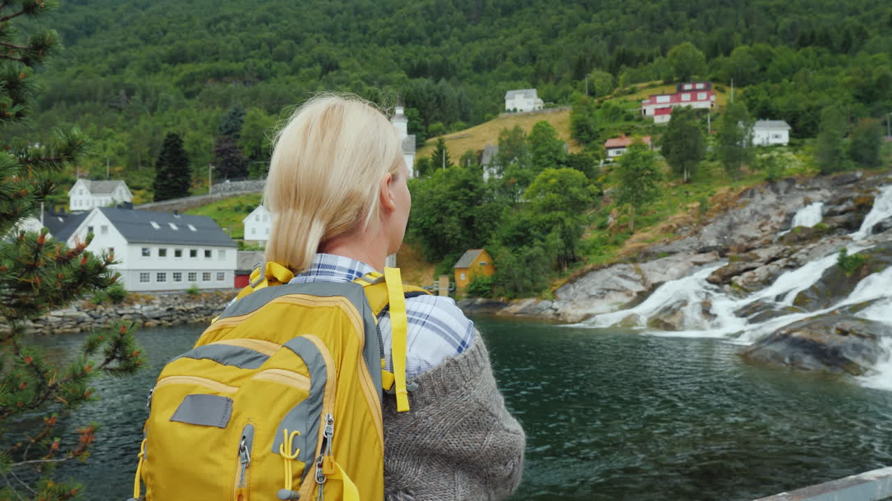 una mujer admira el pueblo noruego y la cascada viajando en escandinavia