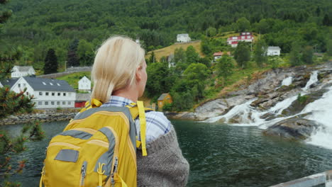 a woman admires the norwegian village and the waterfall travelling in scandinavia