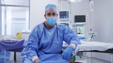 retrato de un cirujano caucásico con máscara facial sentado en el quirófano de un hospital