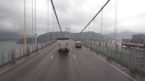 pov driving across the iconic tsing ma bridge in hong kong on a cloudy, wet day.