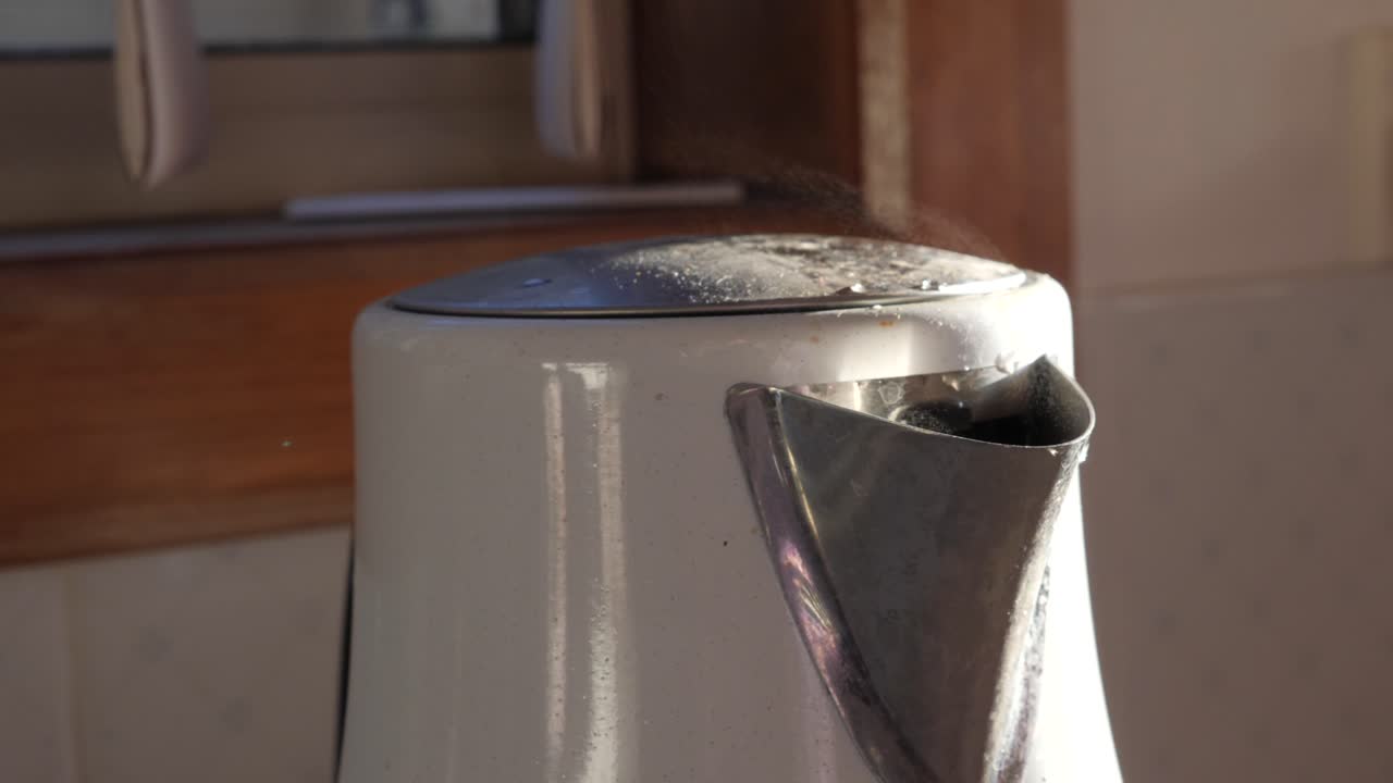 끓는 물 주위를 팬하고 흰색 현대식 주전자에서 증기가 나옵니다.