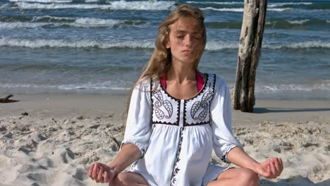 una mujer delgada sentada en la arena haciendo ejercicio de yoga en una meditación pacífica con los ojos cerrados
