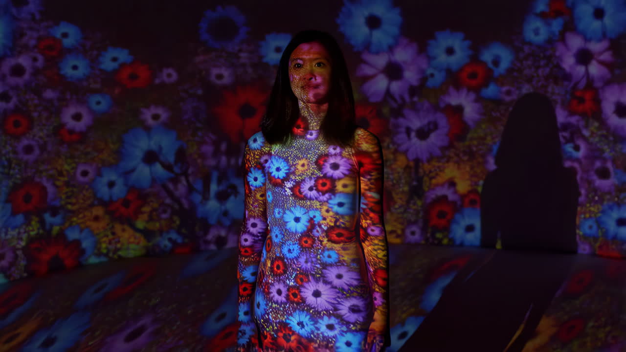 Woman Illuminated by Colorful Flower Projections in an Art Installation