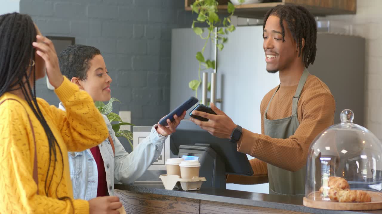 カフェでQRコード決済を利用し、多様な女性の友人のスマートフォンをスキャンする黒人男性バリスタ
