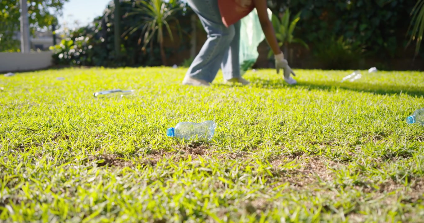 Spotting bottle, female wearing glove walking on lawn bending and collecting litter into green bag